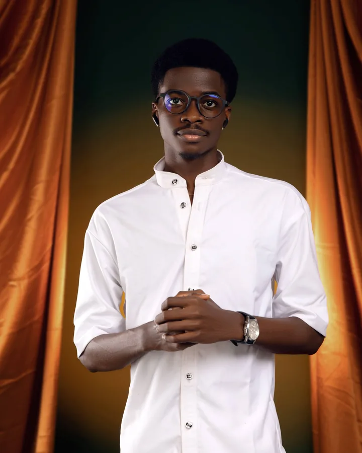 Portrait of Daniel Oluremi in a white shirt against amber curtains